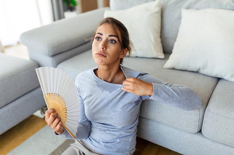 Stressed annoyed woman using waving fan suffer from overheating, summer heat health hormone problem, woman sweat feel uncomfortable hot in summer weather problem without air conditioner