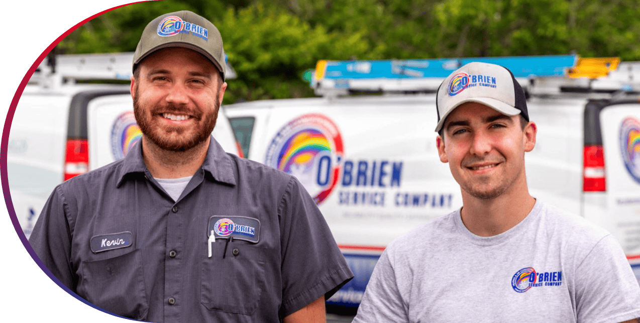 Two O'Brien Service Company employees smiling while in front of HVAC service vehicles.