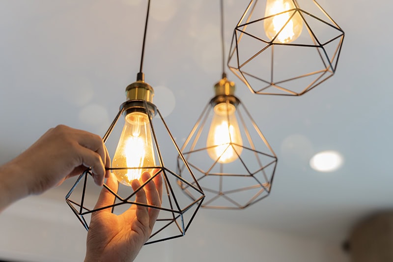 An electrician is installing spotlights on the ceiling. Handyman choosing between energy save and cheap incandescent lamp while changing light in the appartment.