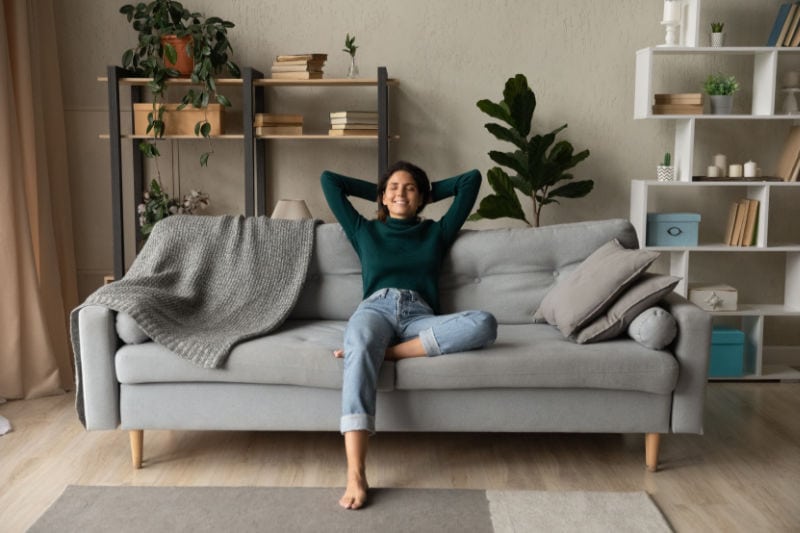 A person with thier hands behind thier head relaxing on a couch.