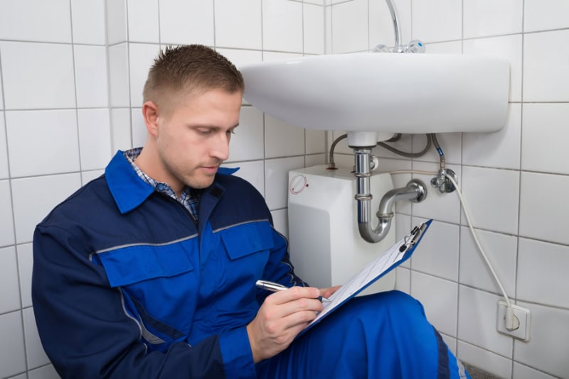 Young Plumber Writing On Clipboard With Pen In Kitchen Room.